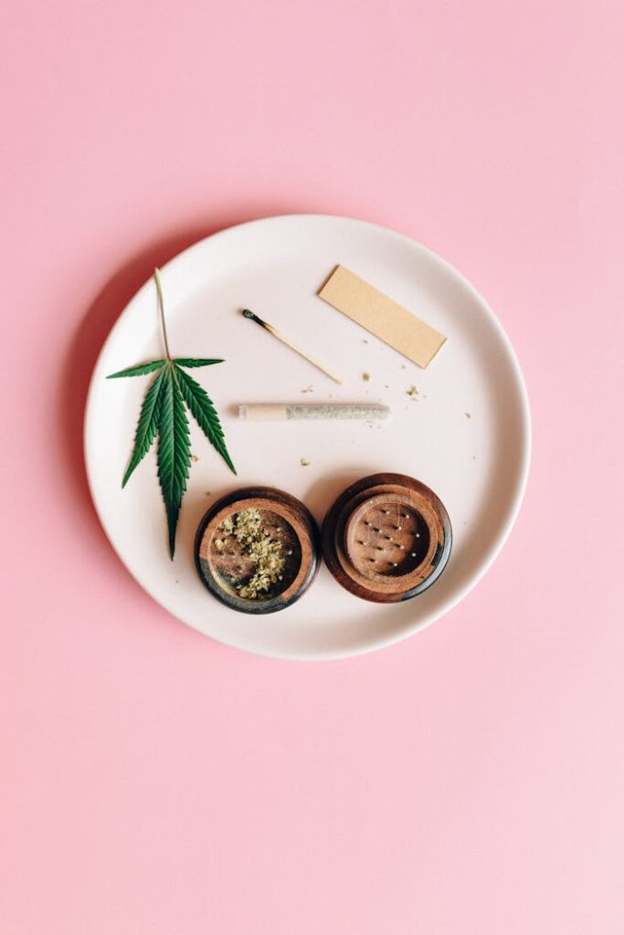 pexels photo 7852642 A cannabis leaf, grinder, and joint on a pink background, symbolizing relaxation.